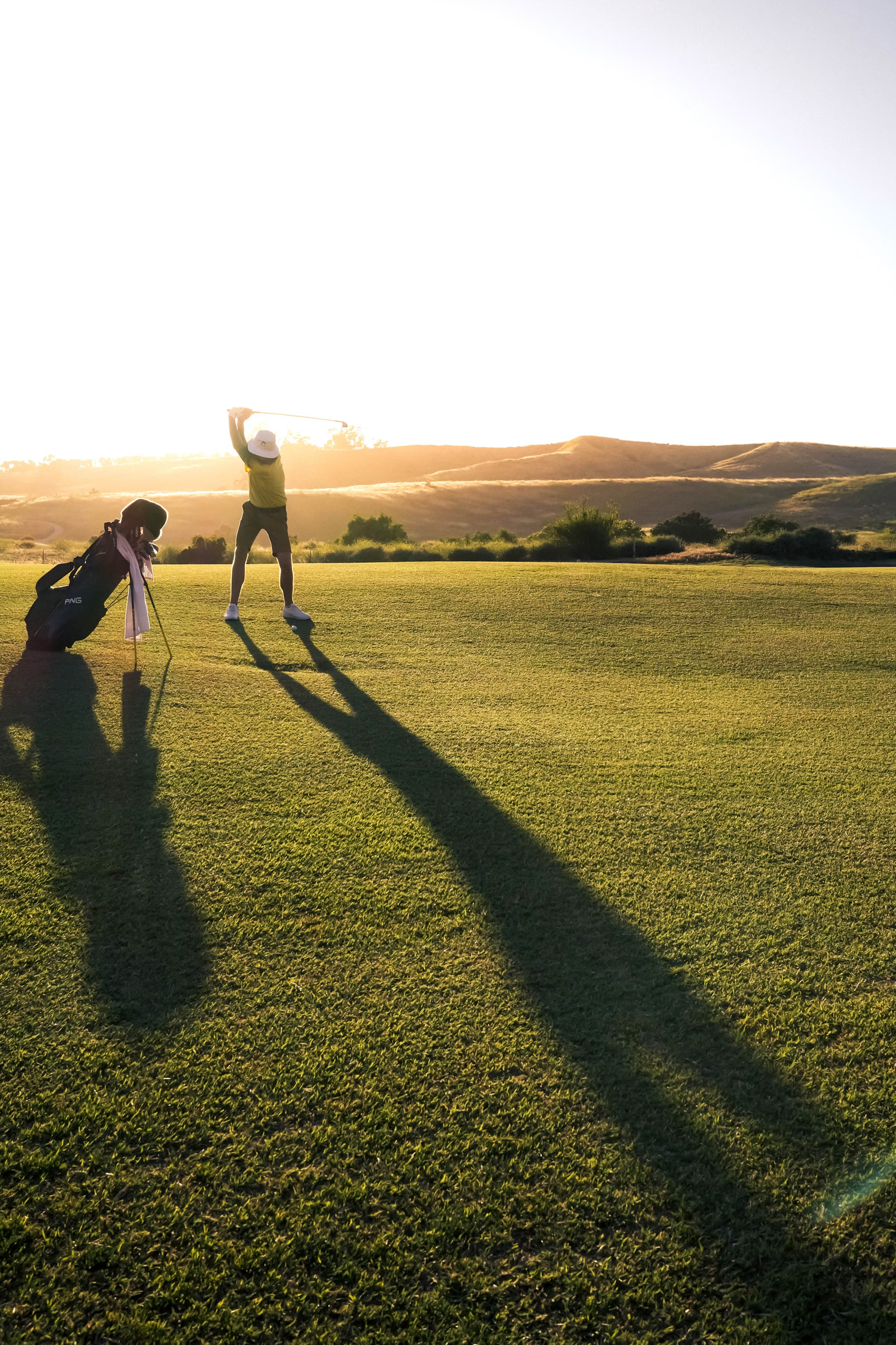 Golfer at sunset on a fairway, long shadow across the green
